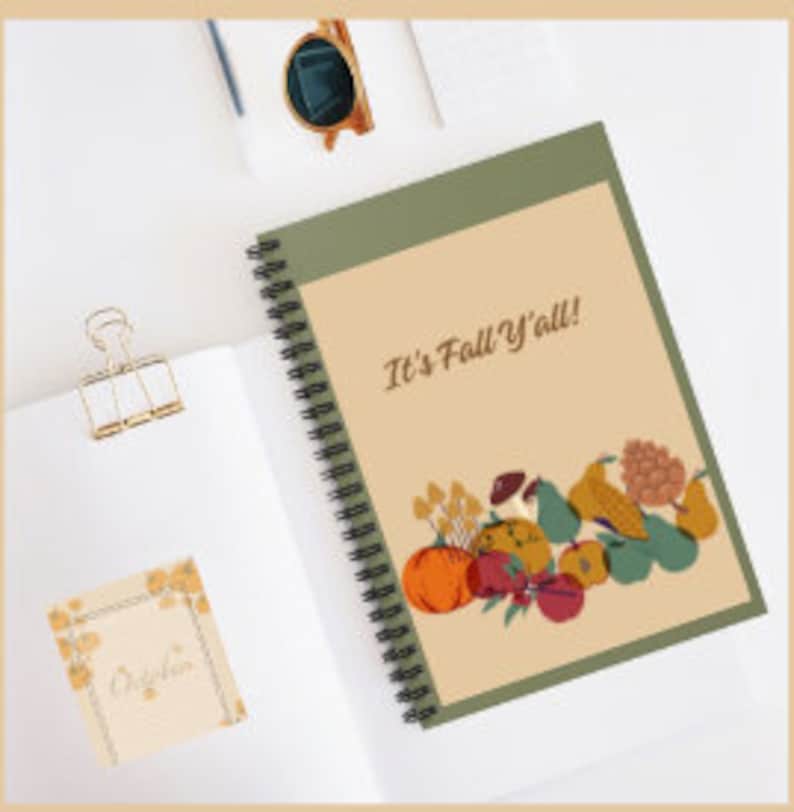 Op de afbeelding: Een spiraalgebonden notitieboek met een groene kaft en de tekst "It's Fall Y'all!" in wit. De kaft heeft een kleurrijke illustratie van herfstfruit en -groenten, waaronder pompoenen, appels, peren en druiven.
