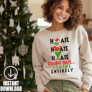 May include: A beige sweatshirt featuring a green Grinch character wearing a Santa hat. The text on the sweatshirt reads "Hate Hate Hate Double Hate... Loathe Entirely".