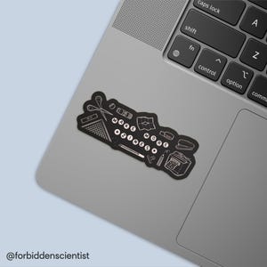 Könnte beinhalten: Schwarzer Aufkleber mit weißen Illustrationen von Bastelwerkzeugen und dem Text "MAKE MORE ZINES". Der Aufkleber enthält eine Schere, eine Karte und einen Tacker. Er befindet sich auf einem grauen Laptop.