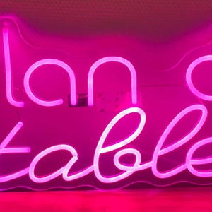 Peut inclure: Enseigne au néon rose vif avec l'inscription "Plan de table" en écriture cursive. Le signe, en forme de nuage, émet une lueur vive sur un fond sombre. Le tube néon est d'un rose éclatant.
