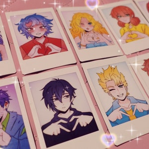 May include: A set of nine illustrated polaroid-style photo cards featuring various characters making a heart shape with their hands. The characters are drawn in a cartoon style and have different hair colours and clothing.