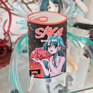 以下が含まれることがあります： 長方形のSaya Mystery Meat缶型ステッカー。女の子が肉片を持っている漫画のイラストが描かれています。「Saya」の文字は赤色、「Mystery Meat」は白色です。ステッカーは500gです。
