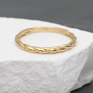 Peut inclure: Une fine bague en or poli présentant un motif de corde torsadée en continu. L'anneau possède une surface métallique lisse et réfléchissante d'un ton or jaune uniforme, arborant une forme circulaire classique avec une texture en spirale.