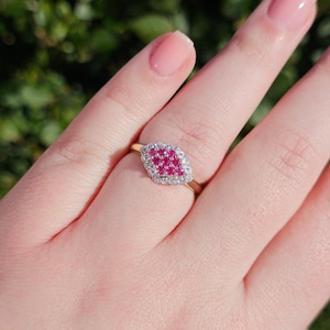以下が含まれることがあります： ピンクのルビーが小さな白いダイヤモンドで囲まれたクラスターがセットされたゴールドリング