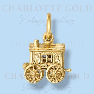 May include: A gold charm in the shape of a horse-drawn wagon with detailed wheels, a small chimney, and side windows. The charm features a top loop for attachment. The text CHARLOTTE GOLD Vintage jewellery is visible in the background.