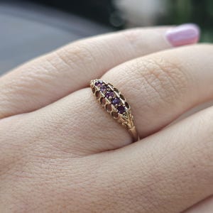 Op de afbeelding: Een gouden ring met een delicaat ontwerp met een rij paarse edelstenen.