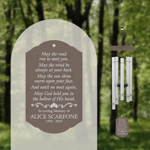 May include: A brown and silver wind chime with a memorial plaque that reads "May the road rise to meet you. May the wind be always at your back. May the sun shine warm upon your face. And until we meet again, May God hold you in the hollow of His hand. In Loving Memory of ALICE SCARFONE 1992-2025"