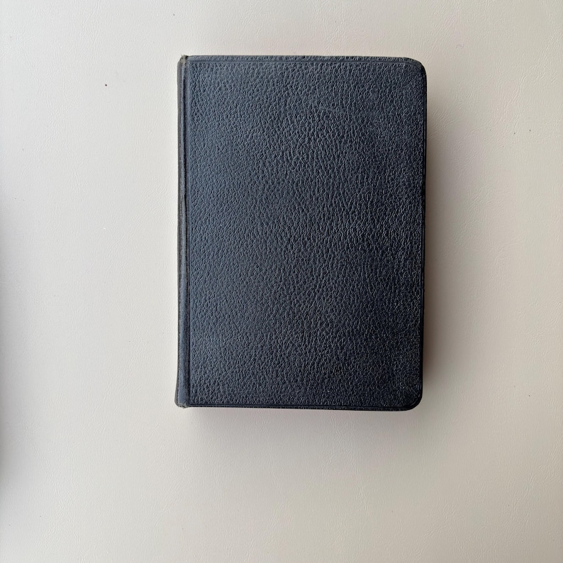 May include: A rectangular book with a dark navy blue cover featuring a textured, pebbled surface. The book is oriented vertically, showing the front cover and the spine edge on the left side. The edges of the cover are rounded at the corners.