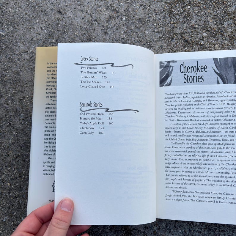 May include: Open book with text about Cherokee and Creek stories. The left page lists "Creek Stories" and "Seminole Stories" with story titles and page numbers. The right page has the title "Cherokee Stories" and detailed text about the Cherokee people.