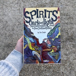 May include: A hardcover book titled "Spirits Dark and Light" with the subtitle "Supernatural Tales from the Five Civilized Tribes" by Tim Tingle. The cover features a colorful illustration of figures in a tribal setting, with a yellow background and bold lettering.