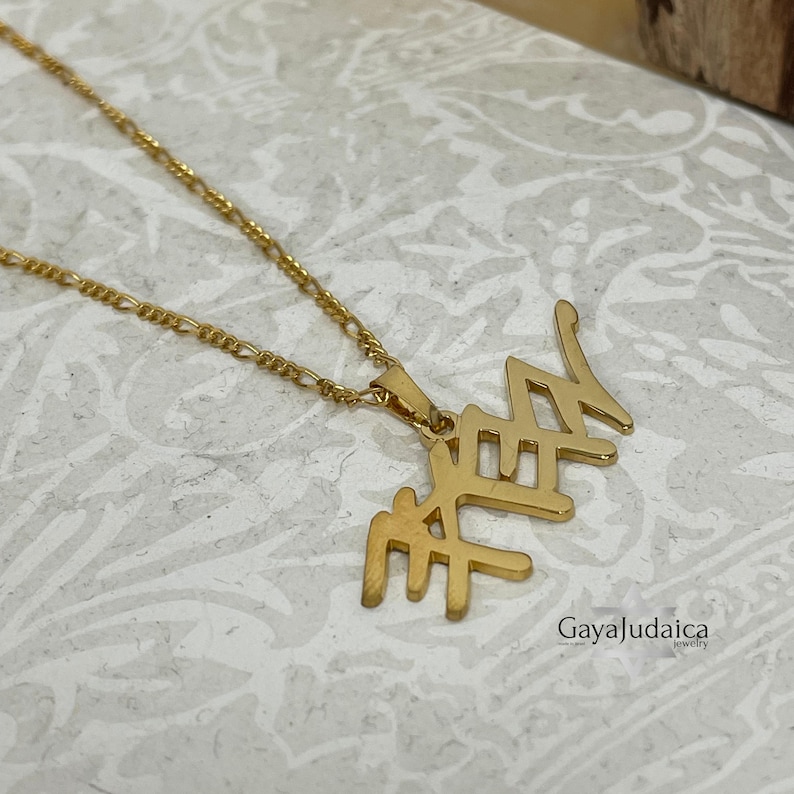 May include: A gold-colored necklace with a pendant featuring Hebrew letters. The necklace has a delicate chain and a pendant with a stylized design. The image includes the text "GayaJudaica jewelry".
