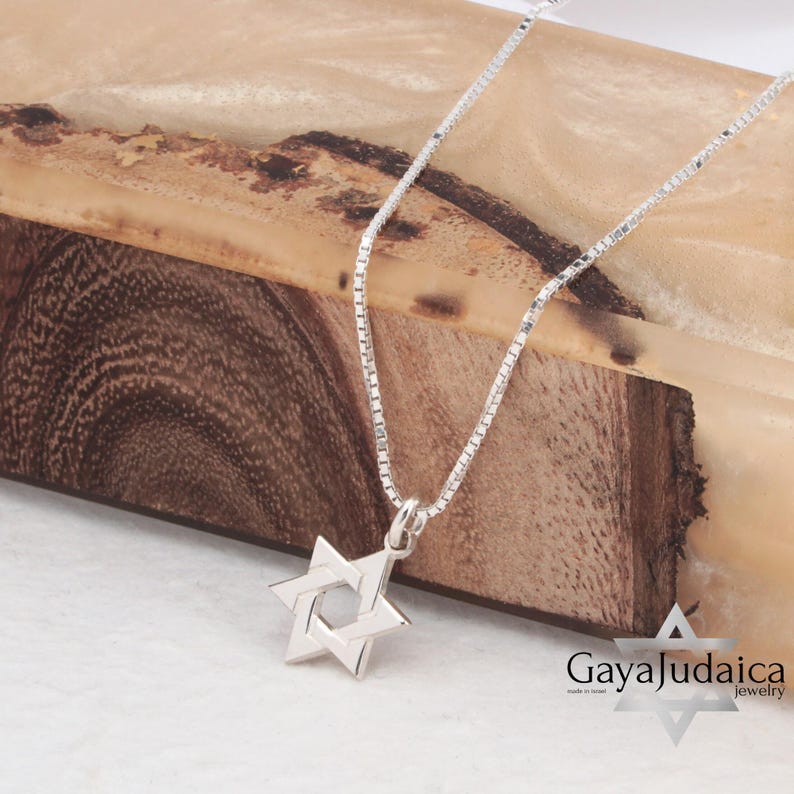 Pu&ograve; includere: Una collana a catena d'argento con un ciondolo a forma di Stella di David in argento. La collana &egrave; su una superficie di legno. Il testo "Gaya Judaica Jewelry" &egrave; visibile nell'angolo in basso a destra dell'immagine.