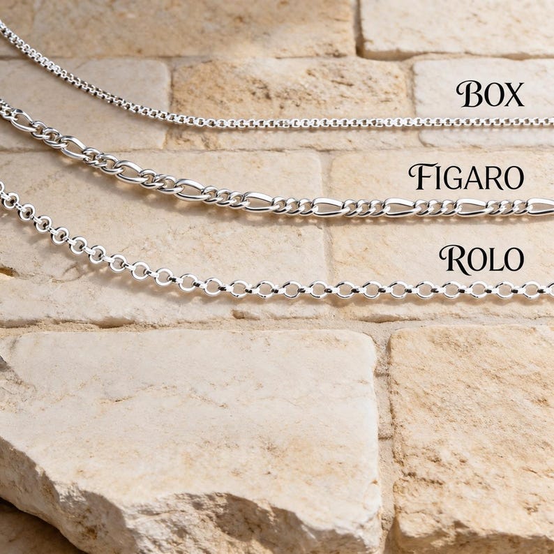 925 sterling silver box, figaro and rolo chains laid across a stone brick wall, a side-by-side comparison of necklace chain styles