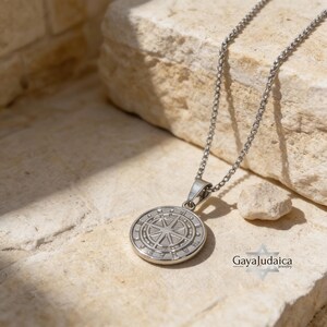 May include: A silver-toned metal necklace featuring a circular pendant with an embossed compass rose design. The pendant hangs from a delicate chain, showcasing a polished finish and intricate radial detailing on the face of the round charm.