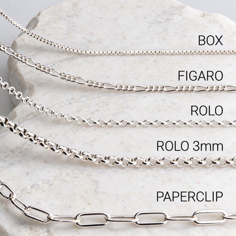 Sterling silver chain comparison on white marble: box, figaro, rolo, 3mm rolo and paperclip necklace chains with labels