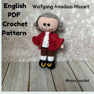 May include: Crochet pattern for an amigurumi doll of Wolfgang Amadeus Mozart. The doll is wearing a red jacket, white shirt, brown trousers, and black shoes. The doll has a grey wig and a smiling face.