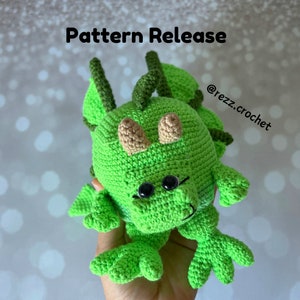 May include: Green crocheted dragon amigurumi toy with black eyes and brown horns. The toy is being held by a hand. The text "Pattern Release" and "@rezz.crochet" are visible in the image.