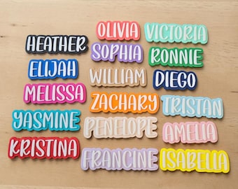 May include: A collection of colorful name tags with white lettering. Names include Heather, Elijah, Melissa, Yasmine, Kristina, Olivia, Sophia, William, Zachary, Penelope, Francine, Victoria, Ronnie, Diego, Tristan, Amelia, and Isabella.