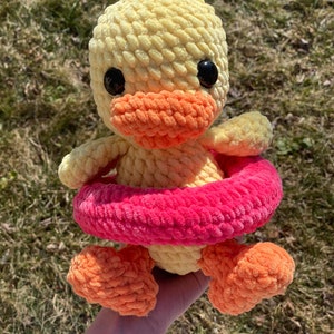 May include: A crocheted yellow duck with orange feet and a pink and orange crocheted life preserver.