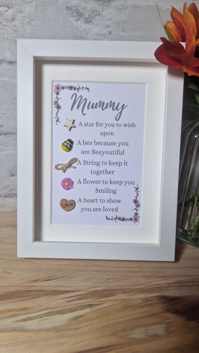Op de afbeelding: Een wit frame met een gedicht erin dat luidt: "Mummy A star for you to wish upon A bee because you are Beeyoutiful A String to keep it together A flower to keep you Smiling A heart to show you are loved". Het gedicht is versierd met een ster, een bij, een touwtje, een bloem en een hart.