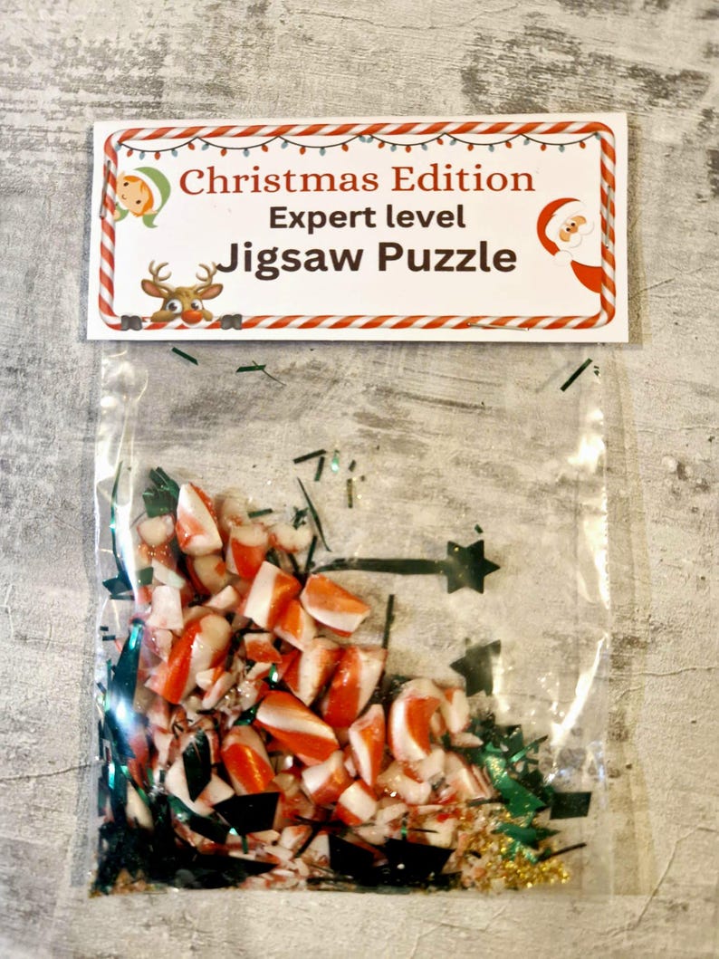 A joke "1,000,000 Piece Christmas style jigsaw puzzle Expert level" gag gift. The product consists of a small, clear bag filled with candy cane, glitter and tinsel, topped with a professional white cardstock label. The label features bold, dark text and a circular icon of a camel in a desert, set against a bright, uncluttered interior background.
