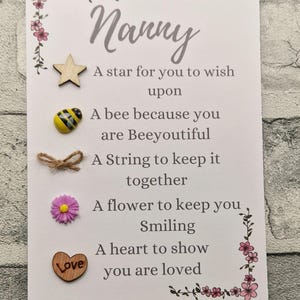 Op de afbeelding: Een witte kaart met het woord "Nanny" in cursief. De kaart heeft een gedicht erop dat zegt: "Een ster om een wens te doen, Een bij omdat je prachtig bent, Een touwtje om het bij elkaar te houden, Een bloem om je te laten glimlachen, Een hart om te laten zien dat je geliefd bent". De kaart heeft een ster, een bij, een touwtje, een bloem en een hart.