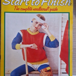 Könnte beinhalten: Ein gelbes und rotes Magazincover mit dem Titel "Start to Finish" und dem Text "The complete needlecraft guide". Das Cover zeigt eine Frau, die einen rot-blau-gelben Pullover, eine blaue Hose und ein weißes Stirnband trägt. Sie hält einen Baseballschläger und einen Baseball.