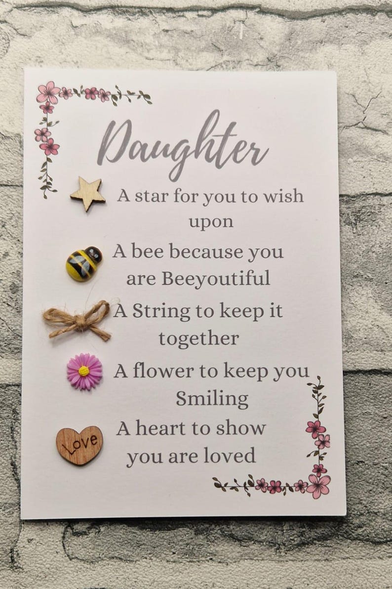 Op de afbeelding: Een witte kaart met een roze bloemrand en de tekst "Daughter" in een cursief schrift. De kaart heeft een ster, een bij, een touwtje, een bloem en een hart met het woord "Love" erop. De kaart heeft ook de tekst "A star for you to wish upon", "A bee because you are Beeyoutiful", "A String to keep it together", "A flower to keep you Smiling", "A heart to show you are loved".