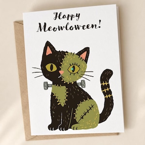 May include: A white greeting card featuring the text Happy Meowloween! and an illustration of a black cat with olive green patches, stitched details, and two grey bolts on its neck, resembling a monster character with yellow eyes.