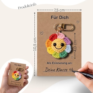 Puede incluir: Un llavero de flor de ganchillo hecho a mano y colorido con una cara sonriente, sujeto a un cierre dorado. El llavero est&aacute; en una tarjeta marr&oacute;n de 10,5 cm x 7,5 cm con el texto "F&uuml;r Dich" y "Als Erinnerung an: Deine Klasse 46".