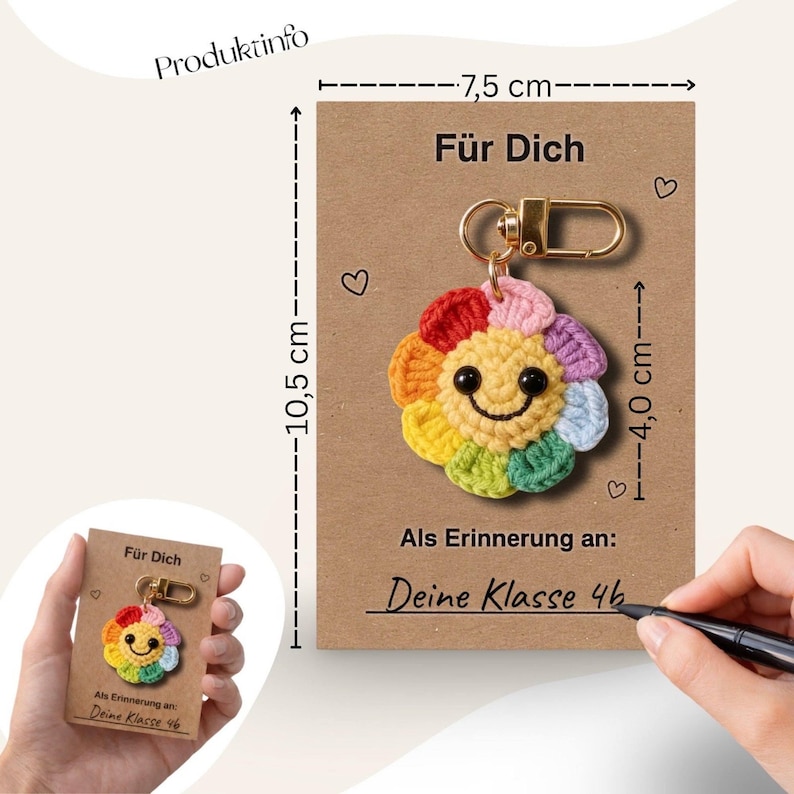 Puede incluir: Un llavero de flor de ganchillo hecho a mano y colorido con una cara sonriente, sujeto a un cierre dorado. El llavero est&aacute; en una tarjeta marr&oacute;n de 10,5 cm x 7,5 cm con el texto "F&uuml;r Dich" y "Als Erinnerung an: Deine Klasse 46".