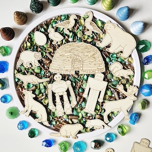 May include: A collection of wooden animal and robot cutouts, including a bear, raccoon, and beaver, arranged around a white plate filled with green and brown decorative elements. Colorful gem-shaped objects surround the plate.
