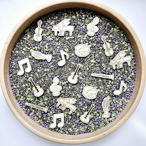 May include: A wooden bowl filled with black and purple beads, containing various wooden musical instrument cutouts. Instruments include violins, pianos, guitars, drums, trumpets, and musical notes. The bowl is made of light-colored wood.