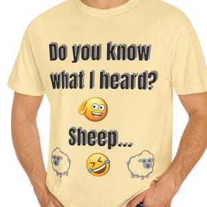 May include: A light yellow t-shirt with the text "Do you know what I heard?" above the word "Sheep..." and emoji graphics. The shirt has a crew neck and short sleeves. The shirt is made of a soft, comfortable material.
