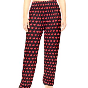 May include: Full-length lounge pants featuring a black base color with a repeating pattern of small, vibrant red hearts distributed evenly across the fabric. The pants have a comfortable elasticized waistband and a straight-leg cut design.