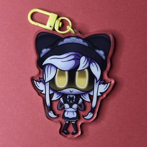 May include: A clear acrylic keychain featuring a cartoon character in a maid outfit. The character has yellow eyes, white hair, and a black and white outfit. A yellow clasp is attached to the top. The background is a solid red.