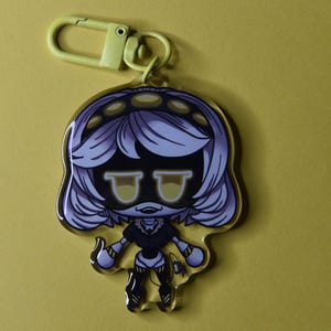 May include: A clear acrylic keychain featuring a cartoon character with white hair, yellow eyes, and a black outfit. The keychain has a yellow clasp and a yellow background.