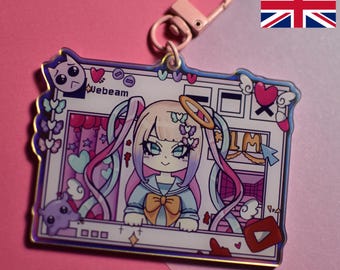 May include: A pink and blue iridescent acrylic keychain featuring a cartoon anime character with pink and blue hair, a halo, and a blue and white sailor uniform. The character is in front of a computer screen with the text "weebeam" and a YouTube logo.