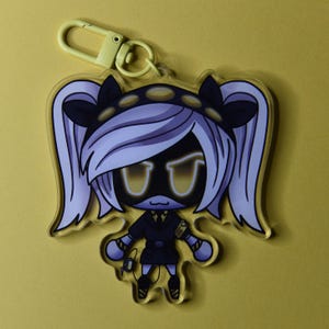 May include: A clear acrylic keychain featuring a cartoon character with white hair, black accents, and yellow glowing eyes. The keychain has a yellow clasp and a yellow background.