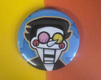 May include: A round button with a cartoon character illustration. The character has black hair, a white face, and wears pink and yellow glasses. The button has a blue background with a star pattern and is set against a yellow and orange background.