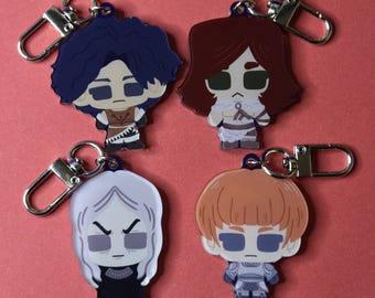 May include: Four character keychains with silver-colored clasps. Each keychain features a cartoon-style character with distinct hairstyles and outfits. The characters have blue, brown, white, and orange hair. The background is a solid red color.