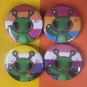 May include: Four circular badges with a green cartoon alien design. Each badge features a different background, including pink, orange, yellow, purple, and white, representing various pride flags. The alien is waving with a friendly expression.