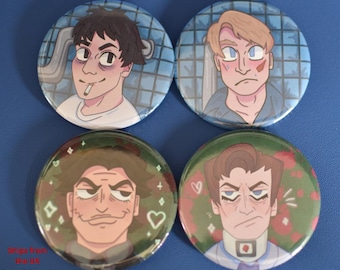 May include: Four round pinback buttons with illustrations of male faces. The top two buttons have a blue background, while the bottom two have green backgrounds. Each button features a different character design with varying expressions and details.