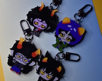 May include: Four cartoon character keychains with black carabiner clips. The characters have yellow horns, and various hair colors including black and blue. The keychains are on a yellow and blue background.