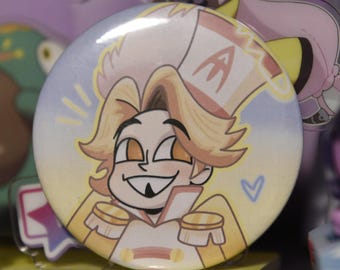 May include: A round button featuring a cartoon character with blonde hair and a white and yellow uniform. The character has a wide grin and is set against a light blue and yellow background. A small blue heart is visible.