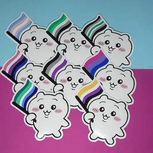 Könnte beinhalten: Eine Sammlung weißer Bärenaufkleber, die jeweils eine Flagge mit verschiedenen LGBTQ+-Pride-Flaggen-Designs halten. Die Aufkleber haben einen Cartoon-Stil mit rosa Wangen und schwarzen Umrissen. Der Hintergrund ist in Blau und Pink geteilt.