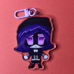 May include: A purple and black cartoon character keychain with a purple clasp. The character has purple hair, a black hat, and a black outfit. The character's eyes are purple rectangles. The keychain is made of clear acrylic.