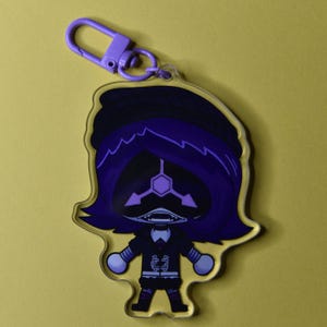 May include: A clear acrylic keychain featuring a cartoon character with purple hair and a black outfit. The character has a geometric face design and is attached to a purple clasp.