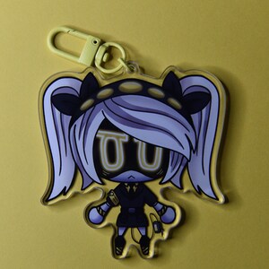 May include: A clear acrylic keychain featuring a cartoon character with white hair, black accents, and yellow highlights. The character has a black outfit and a yellow clasp. The background is a solid yellow.