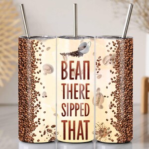 May include: A stainless steel tumbler with a straw, featuring a coffee-themed design. The tumbler is decorated with coffee beans and the phrase "BEAN THERE SIPPED THAT" in a brown font. The background has a light beige colour.